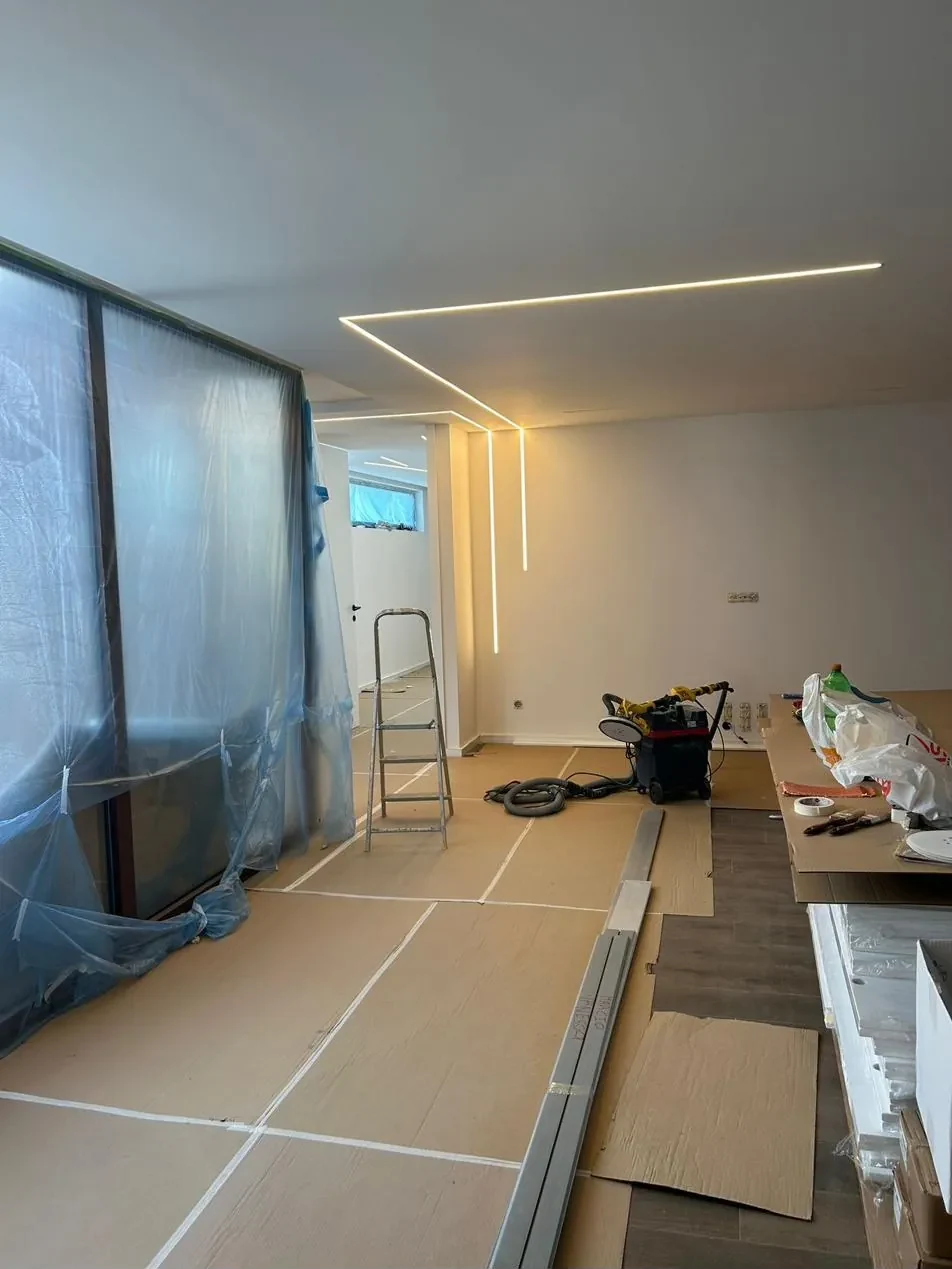 Sala em obra com perfis LED no teto e na parede e chão protegido com cartão