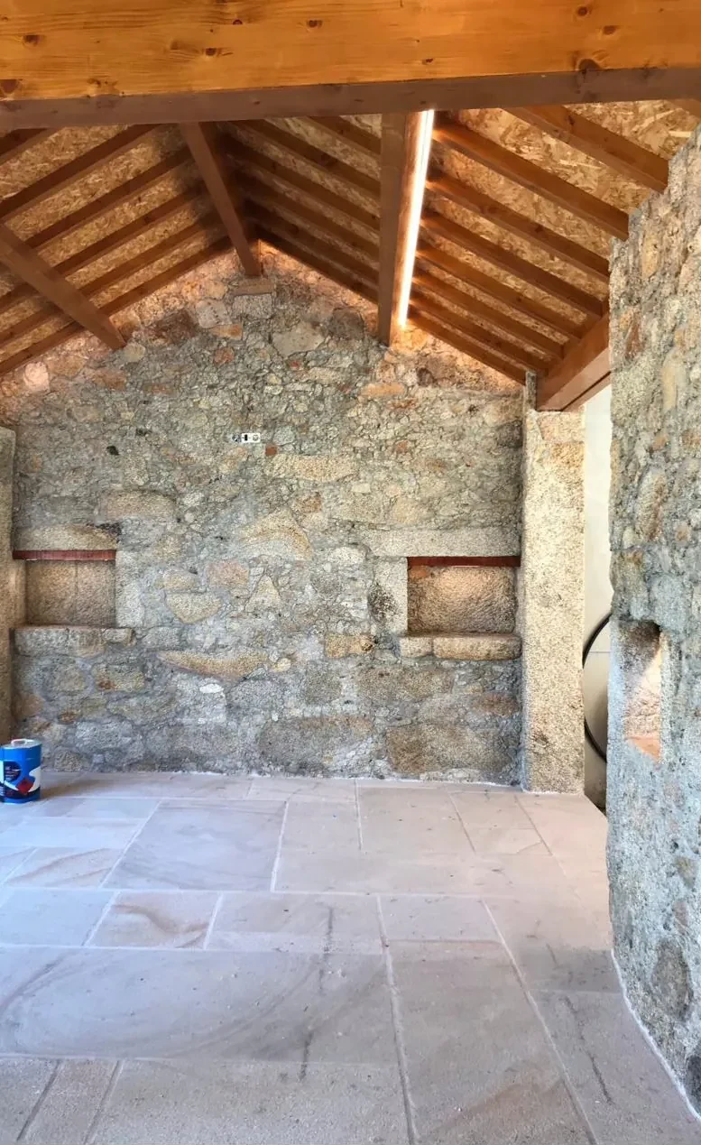 Espaço com paredes em granito e teto em madeira, fita LED vertical na viga e nichos iluminados